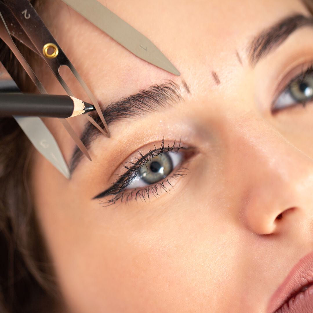 Rojin of Rouge Ink stencils the outline of a female client's eyebrows.