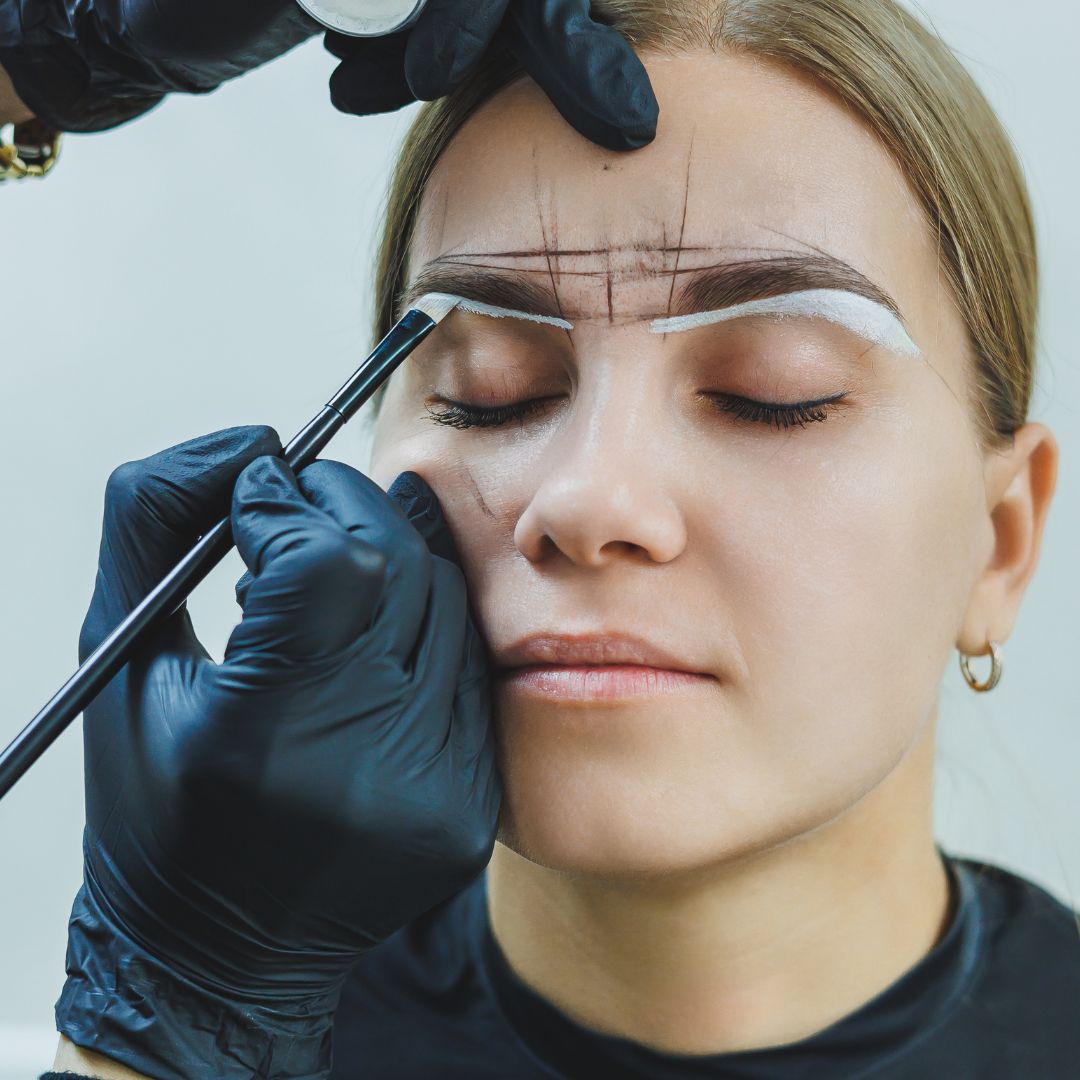 Rojin of Rouge Ink stencils the outline of a female client's eyebrows.
